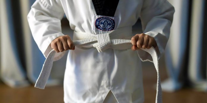 Manos haciendo el nudo del cinturón de un mono de Taekwondo.